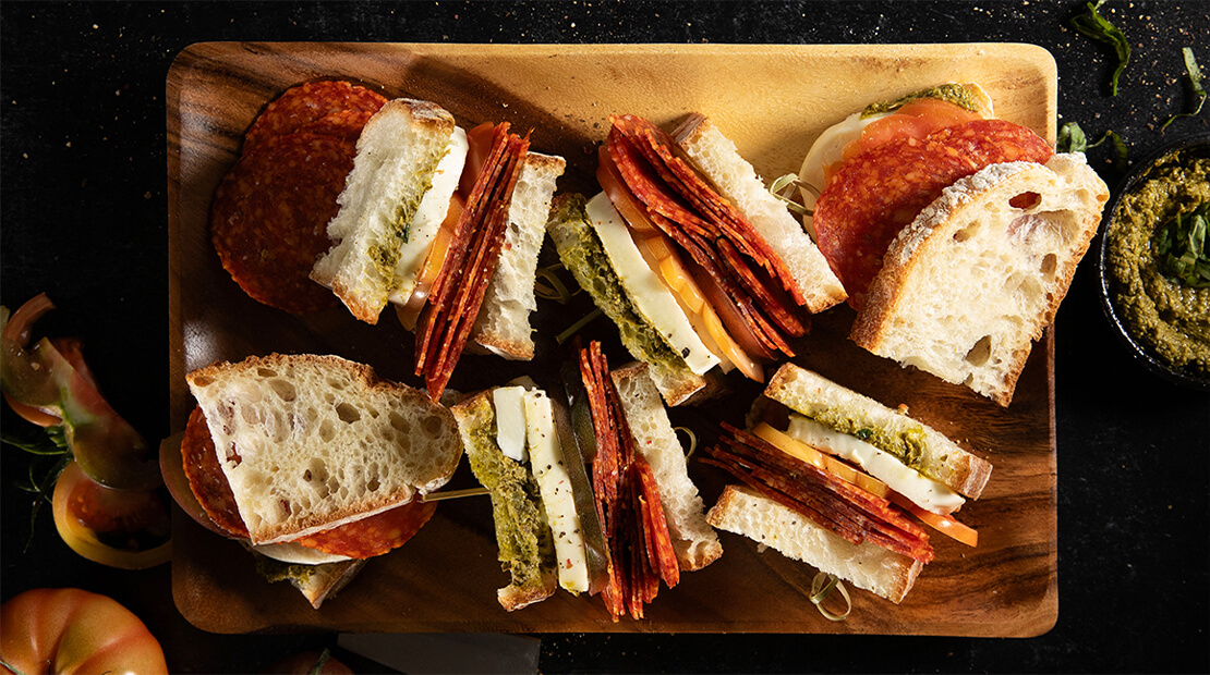 Sliced COLUMBUS® uncured pepperoni sandwiches on a wooden cutting board.
